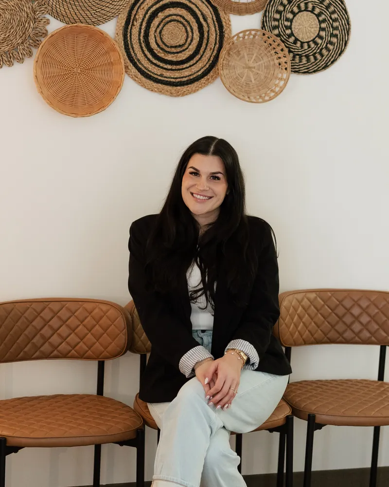 Nina Inclima seated on tan chairs beneath a wall of woven baskets, smiling